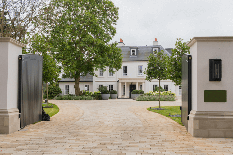 Open gates and brick driveway at the front of a large white house