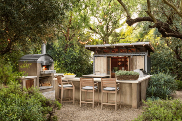 A rustic outdoor kitchen and pizza oven surrounded by trees