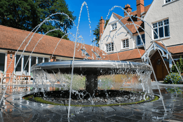 A close up of a fountain spouting water, with a large house in the background